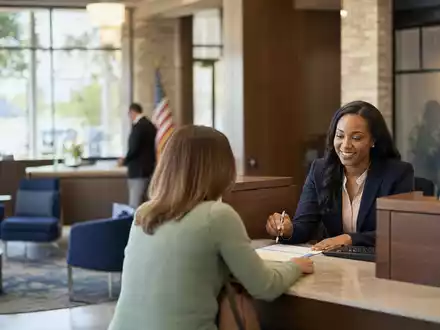 Fotorealistische Bankfiliale zeigt Truist Financial (US89832Q1094) mit Beraterin, Kundin und modernem Empfangstresen im Sonnenlicht - Foto: THN