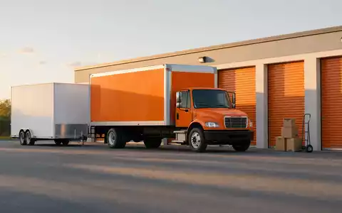 Fotorealistisches Bild von U-Haul Holding Co. zeigt Umzug-LKW und Anhänger vor Lagerhalle, ISIN US02744A1097 - Foto: THN