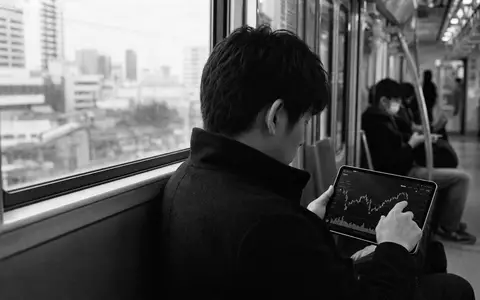 Robinhood Markets US7707031024 dokumentiert in Schwarzweiß einen jungen Investor beim mobilen Aktienchart-Check in der Bahn - Foto: THN
