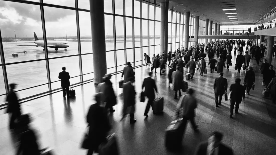 Schwarzweiß-Reportage bewegter Reisender im Flughafenterminal mit Blick auf Startbahn und Flugzeug