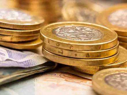 Quilter plc Finanzsektorbasis im Makro: beleuchtete britische Münzen und Banknoten, ISIN GB00BMV92D64, detailreich fotografiert - Foto: THN