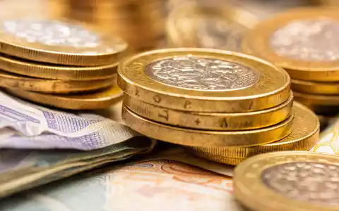 Quilter plc Finanzsektorbasis im Makro: beleuchtete britische Münzen und Banknoten, ISIN GB00BMV92D64, detailreich fotografiert - Foto: THN