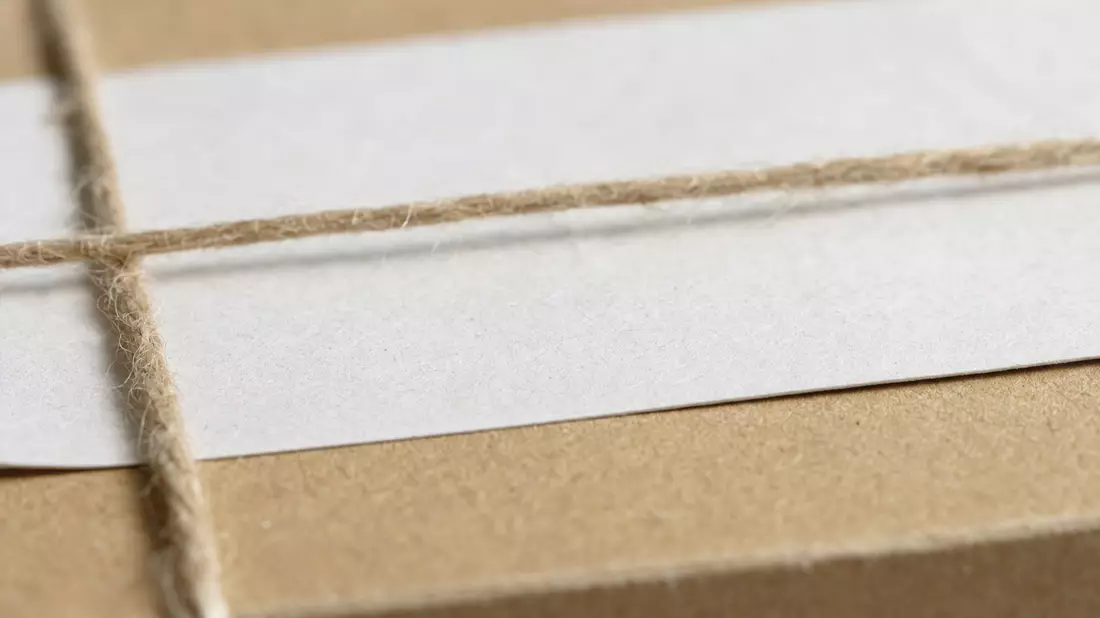 Makroaufnahme von Kartonoberfläche mit Etikettenpapier und gespannter Paketschnur