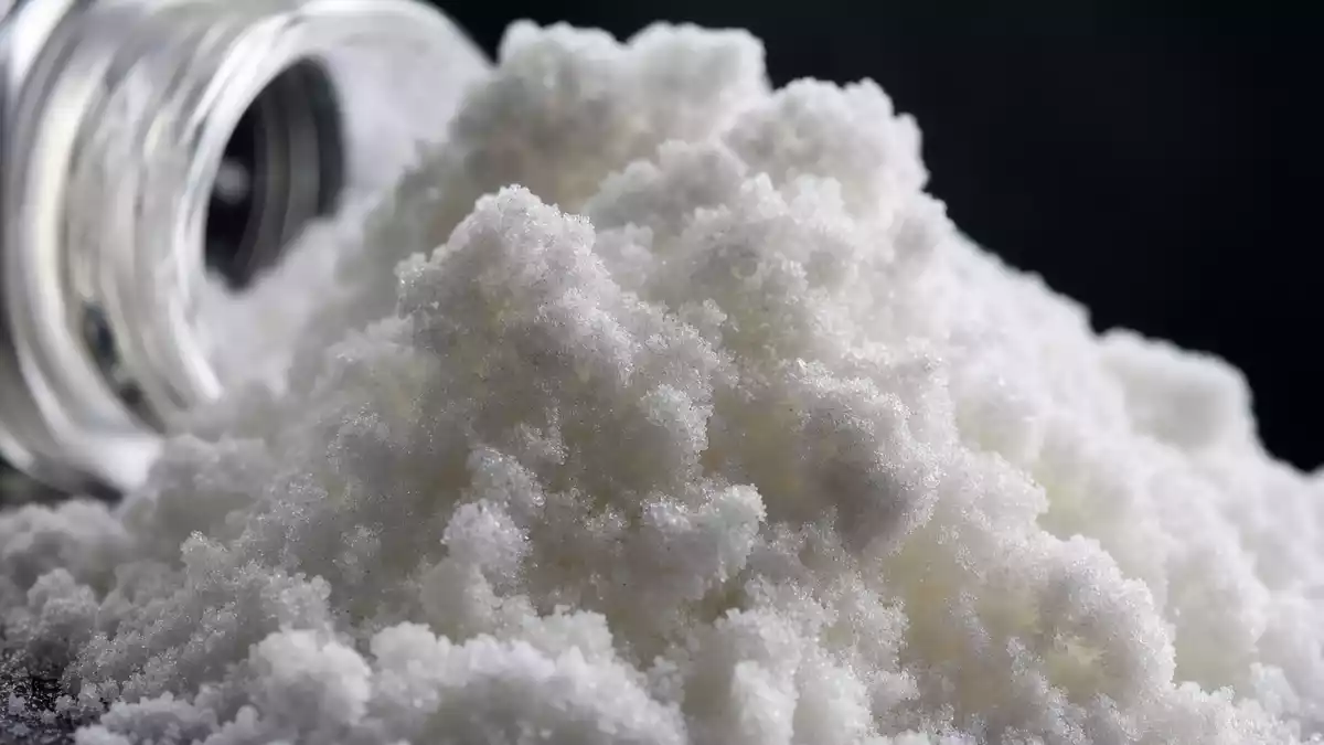 Makroaufnahme von weißem kristallinem Peptidpulver neben einem Glasfläschchen