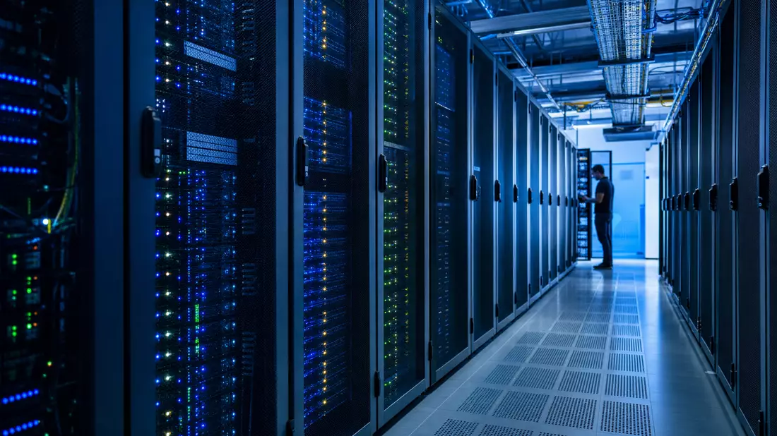 Rechenzentrum mit Serverracks und blauem Licht, Techniker prüft Systeme
