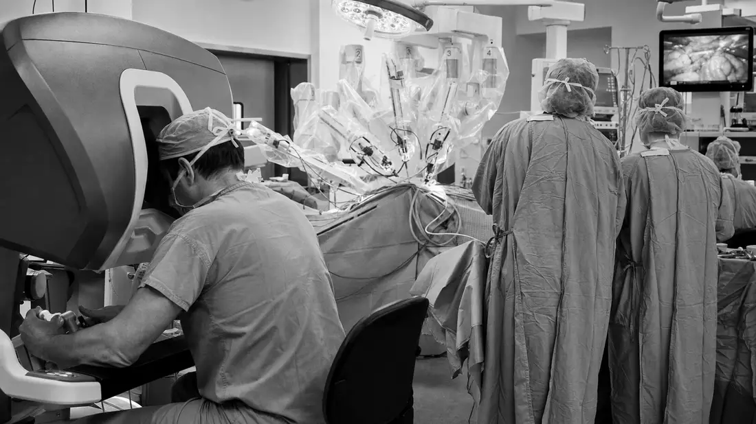 Schwarzweiß-Reportagefoto eines Chirurgen an der Konsole während einer robotergestützten Operation