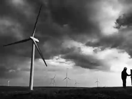 NextEra Energy Inc. (US65339F1012): Schwarz-Weiß-Reportagefoto eines Technikers bei Windturbinen unter dramatischem Wolkenhimmel - Foto: THN