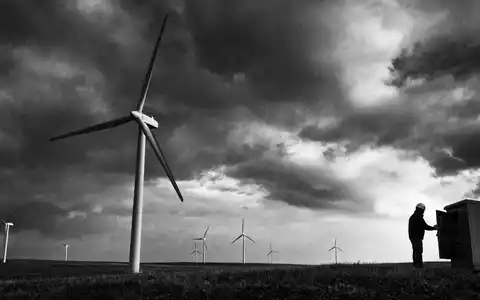 NextEra Energy Inc. (US65339F1012): Schwarz-Weiß-Reportagefoto eines Technikers bei Windturbinen unter dramatischem Wolkenhimmel - Foto: THN