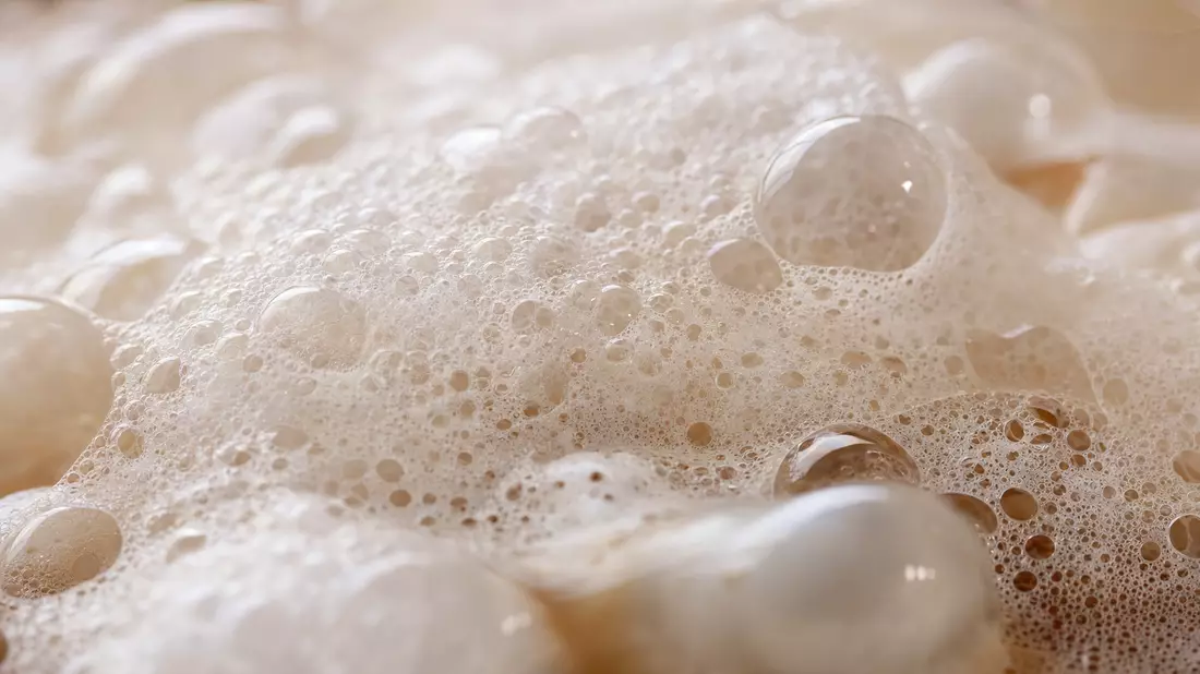 Extreme Makroaufnahme von cremigem Seifenschaum mit feinen glänzenden Wassertröpfchen
