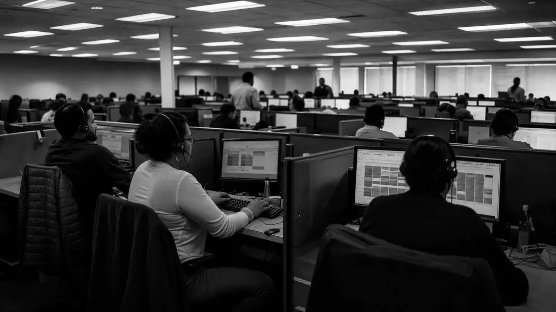 Schwarzweiß-Reportage eines großen Call-Centers mit Mitarbeitern an Planungsbildschirmen