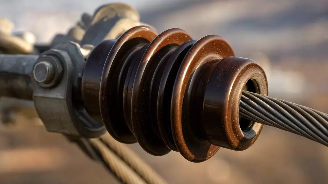 Extreme Makroaufnahme eines braunen Keramikisolators mit Stahlkabeln und Bokeh-Hintergrund