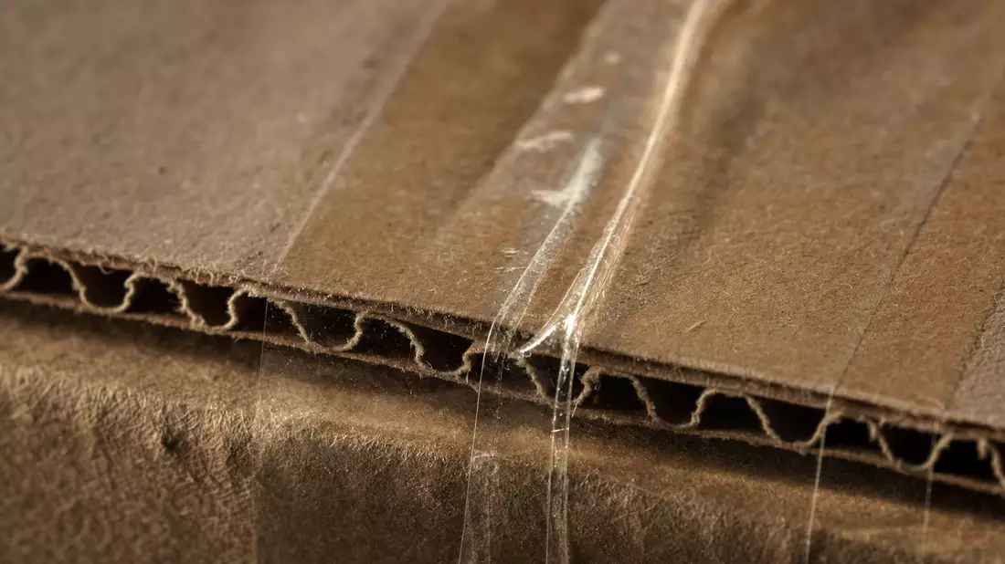 Extreme Nahaufnahme von Wellpappe mit transparentem Klebeband in warmem Streiflicht