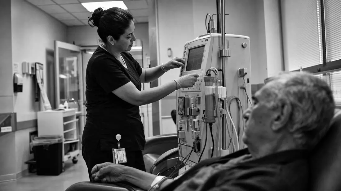 Schwarzweißfoto einer Pflegekraft, die ein Dialysegerät neben einem Patienten bedient