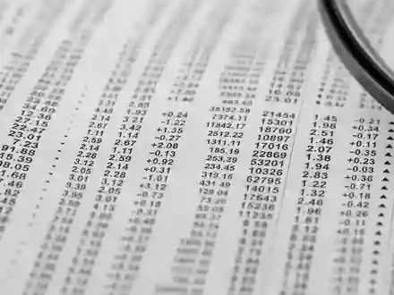 S&P Global Inc. (ISIN US78378X1072): Makroaufnahme von dichten Finanzzeitungstabellen mit Zahlen und Lupe am Rand - Foto: THN