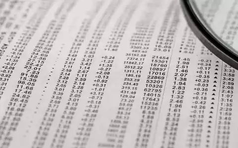 S&P Global Inc. (ISIN US78378X1072): Makroaufnahme von dichten Finanzzeitungstabellen mit Zahlen und Lupe am Rand - Foto: THN