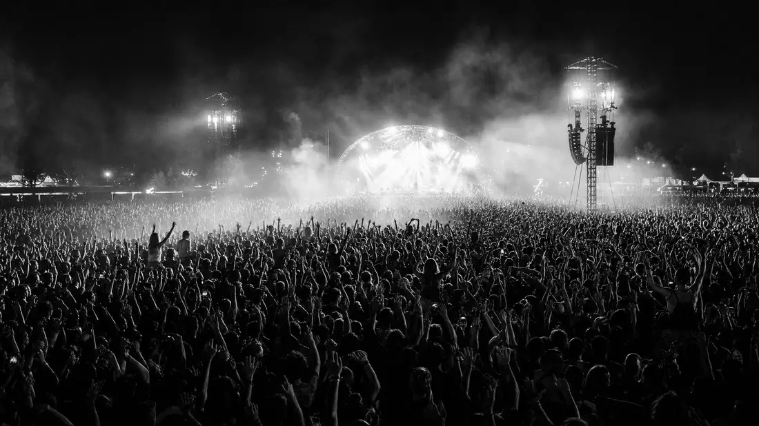 Schwarz-Weiß Reportagefoto einer riesigen Festivalmenge vor beleuchteter Freiluftbühne