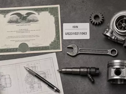 Cummins Inc. Flatlay US2310211063 – Draufsicht auf Aktien-Zertifikat, ISIN-Karte und branchentypische Motorenteile - Foto: THN