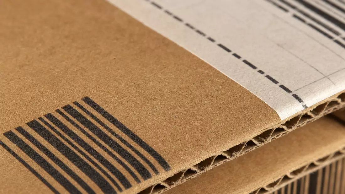 Extreme Makroaufnahme von Wellpapp-Kartonoberfläche mit Barcode-Aufdruck und Klebebandstreifen