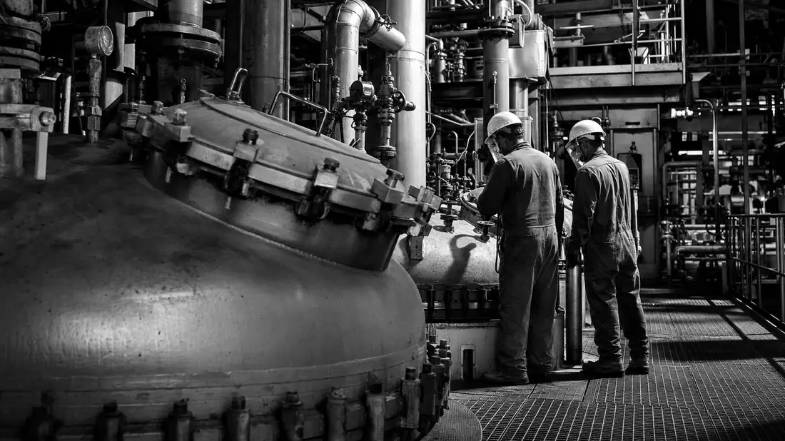 Schwarzweiß-Reportagebild von Industriearbeitern bei der Inspektion chemischer Reaktorbehälter