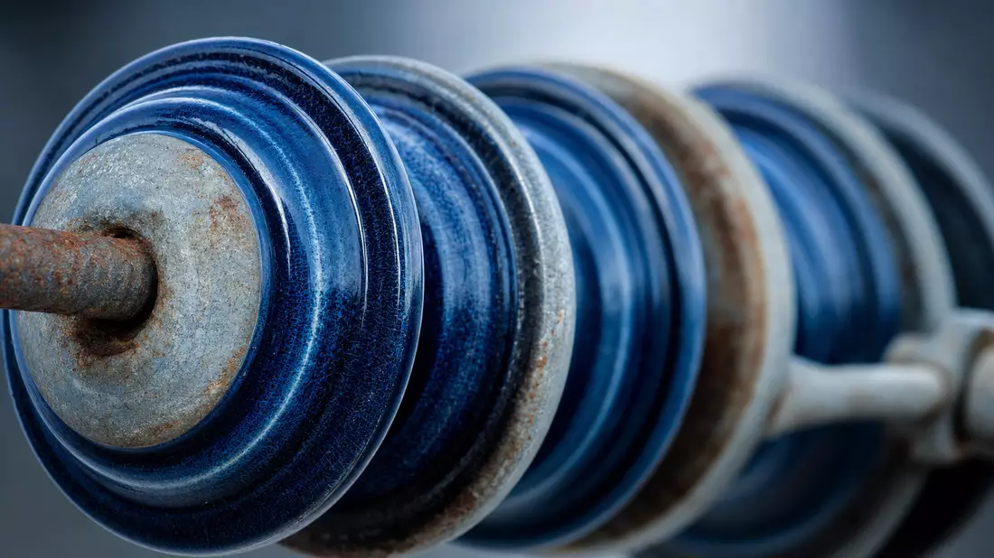 Extreme Makro-Nahaufnahme blauer Hochspannungs-Keramikinsulatoren mit Metallkappen und Patina