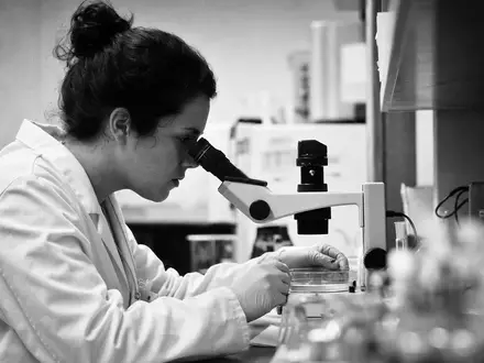 Vertex Pharma US92532F1003 dokumentiert eine Forscherin beim Mikroskopieren in dokumentarischer Schwarzweiß-Reportage-Optik im Labor - Foto: THN