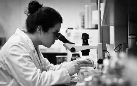Vertex Pharma US92532F1003 dokumentiert eine Forscherin beim Mikroskopieren in dokumentarischer Schwarzweiß-Reportage-Optik im Labor - Foto: THN