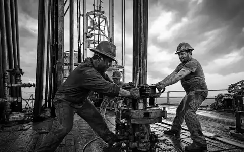Devon Energy US25179M1036 SchwarzweiĂź-Reportage von Arbeitern auf einer Ă–l-Bohrplattform bei stĂĽrmischem Wetter - Foto: THN