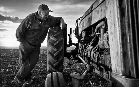 Deere & Co. Landwirt inspiziert Traktor im Schwarzweiß-Reportage-Stil, ISIN US24419L1061 Maschinenbau Dokumentarfoto - Foto: THN