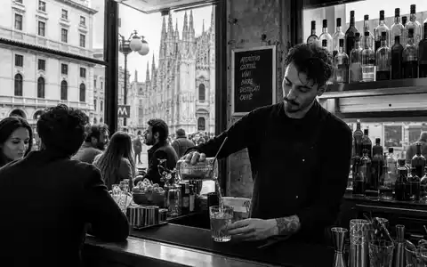 Davide Campari-Milano N.V. (NL0015435975) dokumentiert schwarzweiße Reportage-Aufnahme einer belebten Bar-Szene mit Mailänder Dom im Hintergrund - Foto: THN