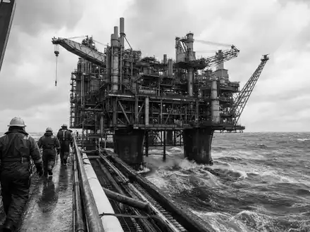 Schwarzweiß-Reportagefoto einer Offshore-Plattform illustriert die Offshore-Förderaktivitäten von Shell plc, ISIN NL0000009827, in rauer See - Foto: THN