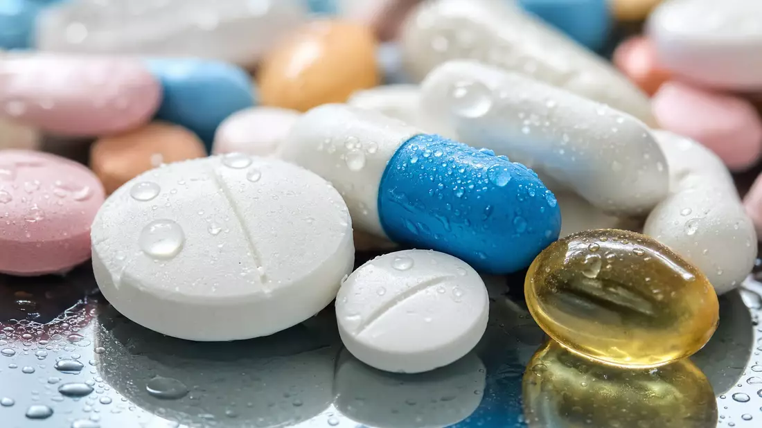 Makroaufnahme bunter Tabletten und Kapseln mit glänzenden Wassertropfen