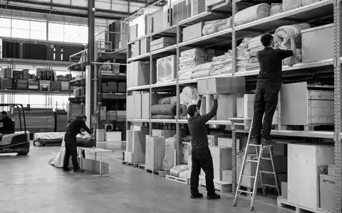 Dunelm Group plc GB0033745292 dokumentiert schwarzweiß Arbeiter in einer großen Textilien-Lagerhalle beim Sortieren - Foto: THN