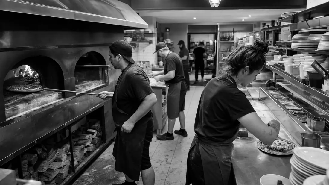Dokumentarische Schwarzweißaufnahme einer geschäftigen Pizzabäckerei-Küche