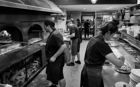 Schwarzweiß-Reportage aus einer Großküche illustriert Domino's Pizza Group plc, ISIN GB0002936932, in der Systemgastronomie-Branche - Foto: THN