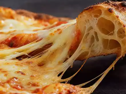 Makroaufnahme von geschmolzenem Käse auf Pizzateig veranschaulicht Domino's Pizza Group plc, ISIN GB0002936932, der Systemgastronomie-Branche - Foto: THN