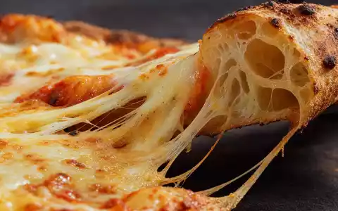 Makroaufnahme von geschmolzenem Käse auf Pizzateig veranschaulicht Domino's Pizza Group plc, ISIN GB0002936932, der Systemgastronomie-Branche - Foto: THN