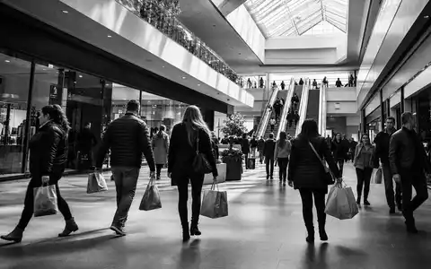 Simon Property Group US8288061091 dargestellt als dokumentarische Schwarzweiß-Reportage mit Käufern in belebter Mall-Passage - Foto: THN