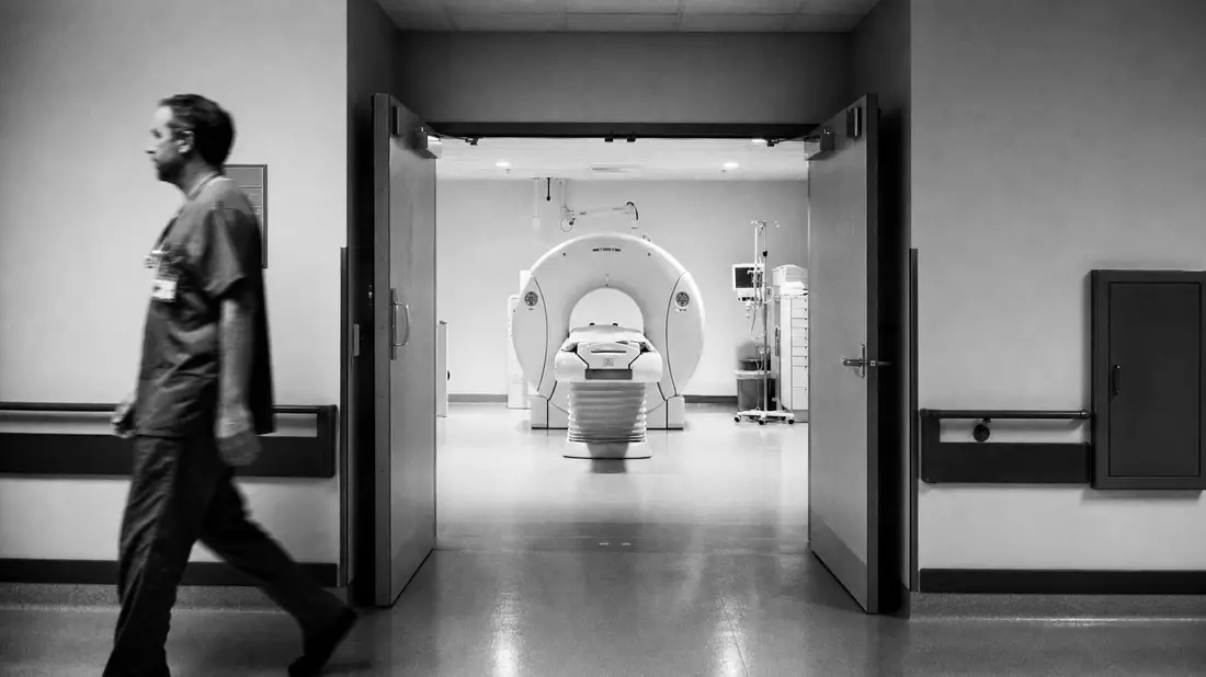 Schwarzweiß-Reportagefoto eines Klinikflurs mit CT-Scanner und Arzt