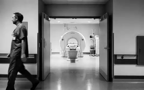 Siemens Healthineers DE000SHL1006 dokumentiert Schwarzweiß-Reportage mit Arzt und unmarkiertem CT-Scanner im Klinikflur - Foto: THN