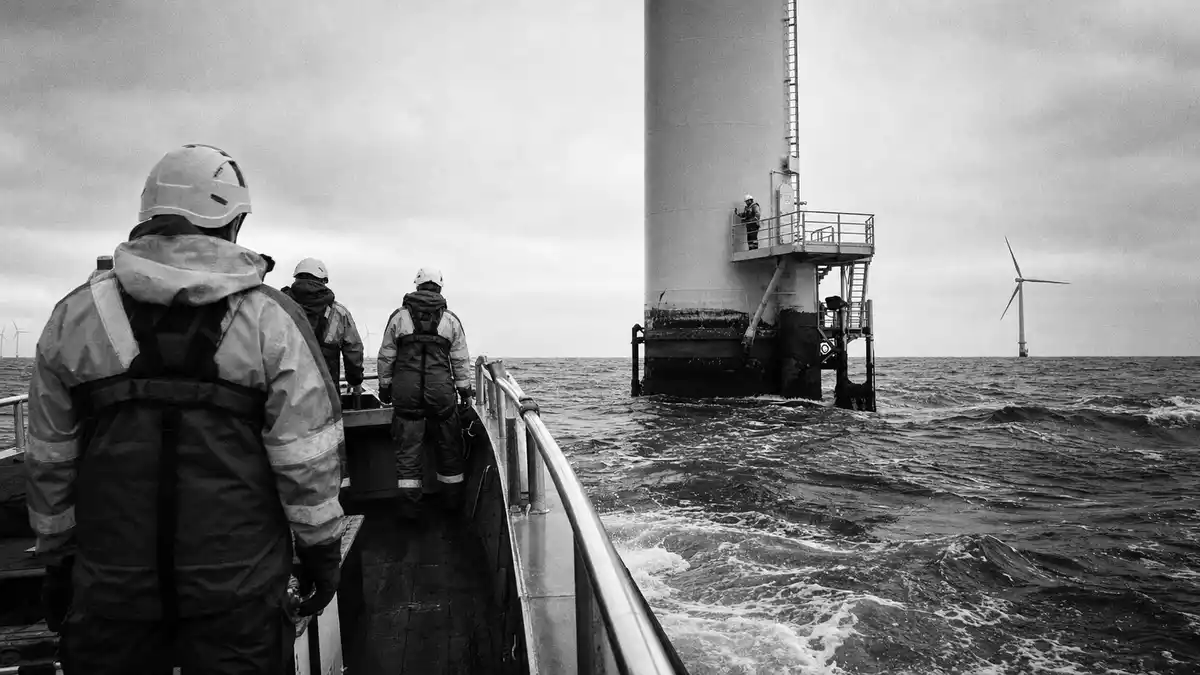 Schwarzweiß-Reportagefoto von Technikern auf einem Boot vor einer Offshore-Windturbine
