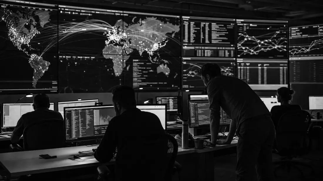 Schwarzweißes Security Operations Center mit Analysten vor Monitorwand