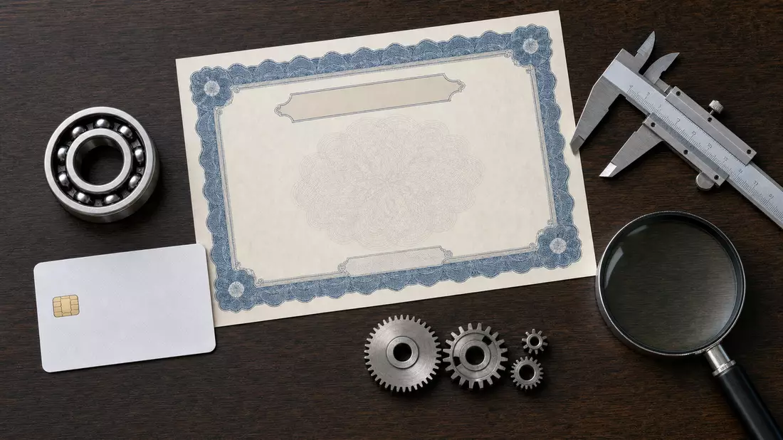 Flatlay mit Aktienzertifikat, ISIN-Karte, Kugellager und Messwerkzeugen auf Holztisch