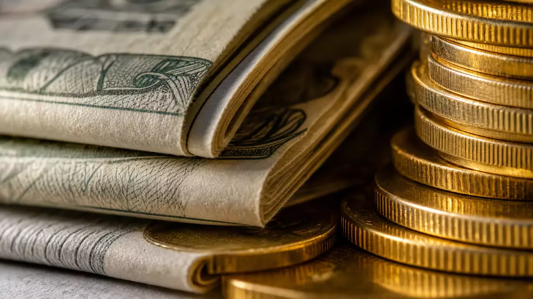 Extreme Nahaufnahme gefalteter Dollarscheine und gestapelter Goldmünzen im Licht