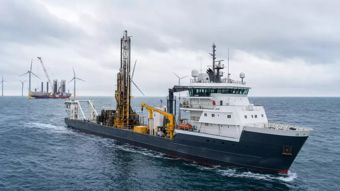 Offshore-Vermessungsschiff mit Bohrturm vor Windpark im grauen Meer