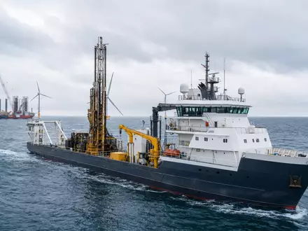 Fugro N.V. (ISIN NL00150004L0) zeigt ein Vermessungsschiff mit Bohrturm nahe einem Offshore-Windpark im grauen Meer - Foto: THN