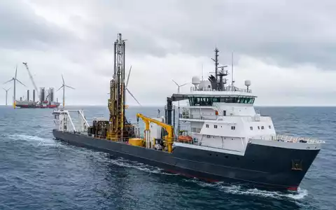Fugro N.V. (ISIN NL00150004L0) zeigt ein Vermessungsschiff mit Bohrturm nahe einem Offshore-Windpark im grauen Meer - Foto: THN