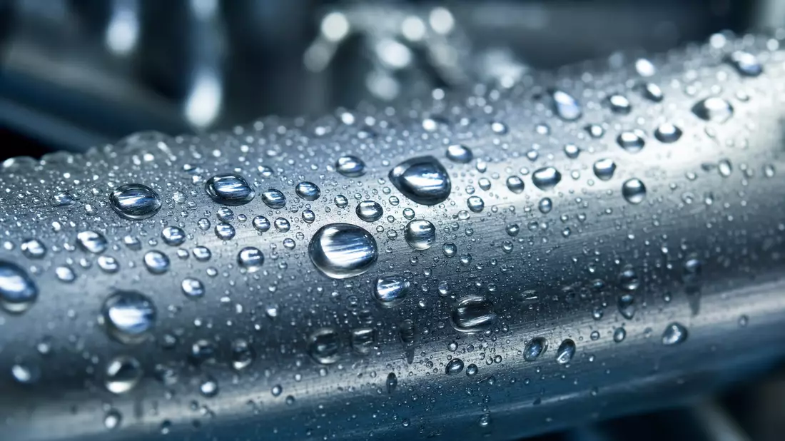 Makroaufnahme glaenzender Wassertropfen auf einer Edelstahl-Rohroberflaeche
