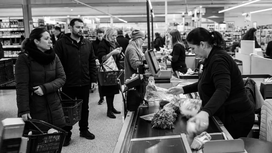 Schwarzweiß-Reportagefoto einer Supermarktkasse mit wartenden Kunden