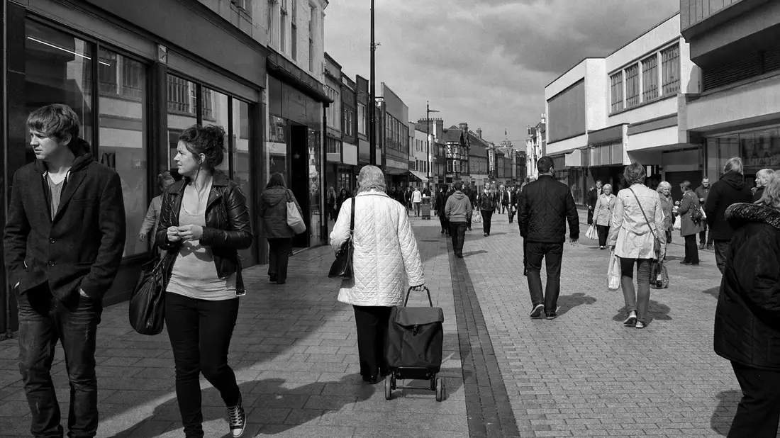 Schwarzweißes Straßenfoto von Passanten auf belebter britischer Einkaufsstraße