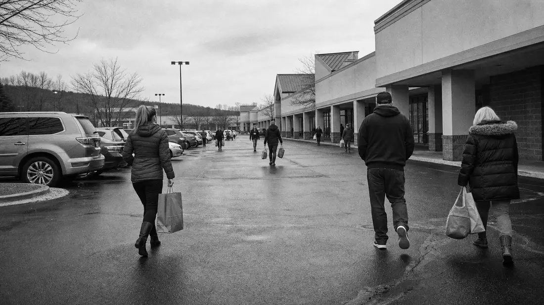 Schwarzweiß-Reportagefoto von Kunden auf einem Parkplatz vor einem Einkaufszentrum